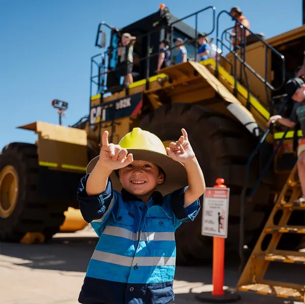 Young boy in hi-vis smiling in front of a cat loader