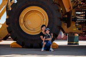 Mother and Son sitting against a cat loaders wheel