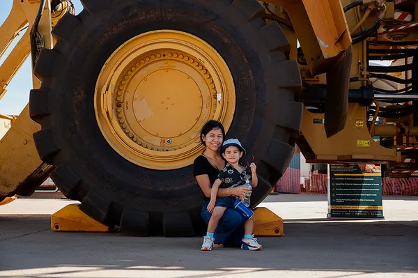 Mother and Son sitting against a cat loaders wheel