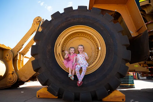 Two sisters sitting in the wheel arch of a Cat Loader